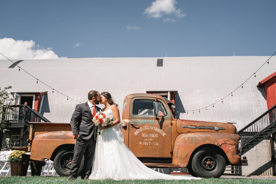 a man and woman kissing in front of a truck during Hayloft on the Arch Wedding