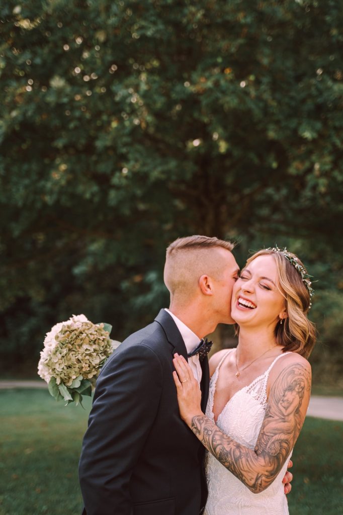 a groom kissing his bride on the cheek for their upstate NY barn wedding